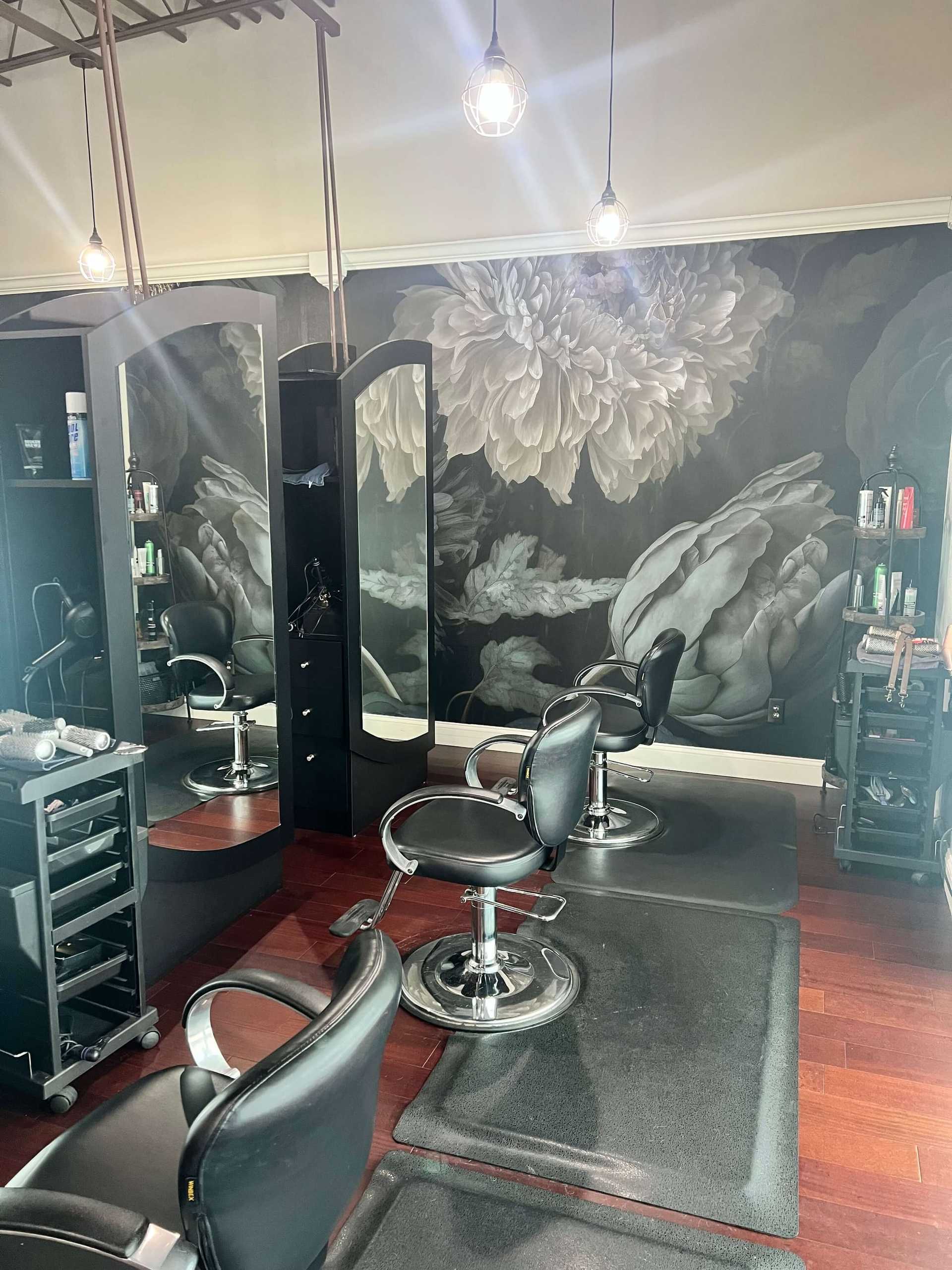 Elegant salon interior with black chairs, floral wall art, and modern lighting fixtures.
