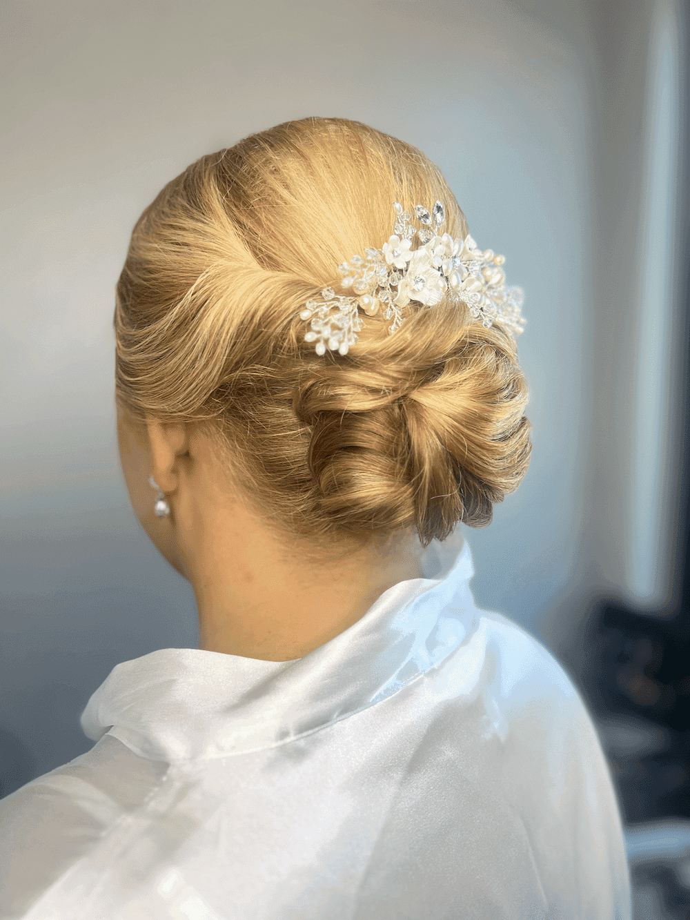 Woman with an elegant updo hairstyle adorned with a jeweled floral hair accessory, wears a white robe.