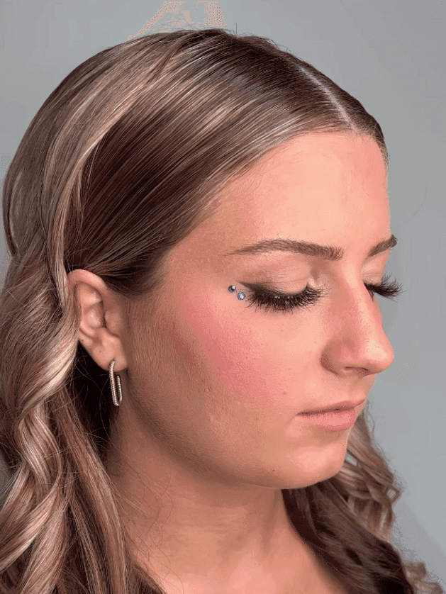 Woman with long hair, eyelash extensions, and facial gem, displayed in side profile.