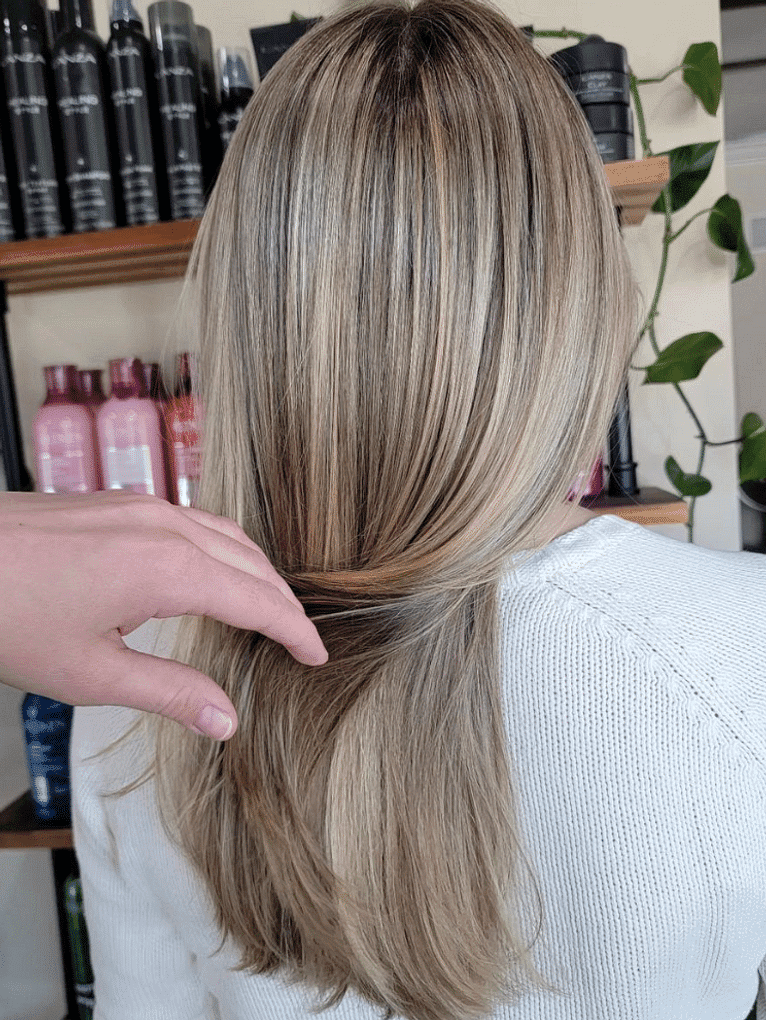 A person with freshly highlighted hair at a salon, stylist adjusting strands for a final look.