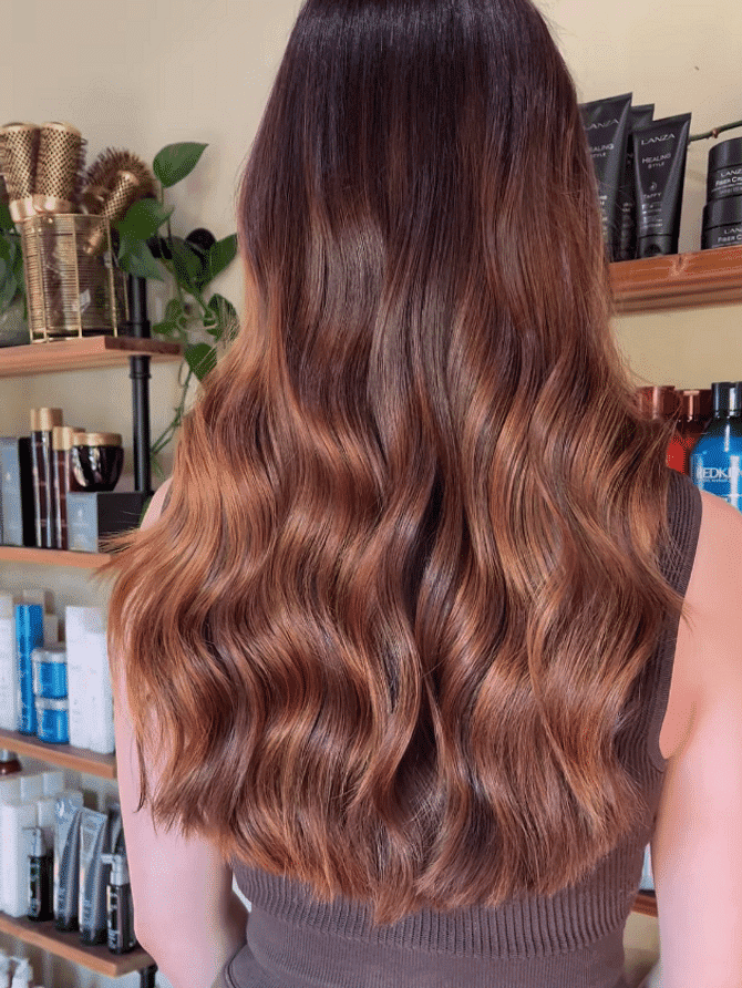 Woman with wavy brown hair stands in front of salon shelves filled with hair products.