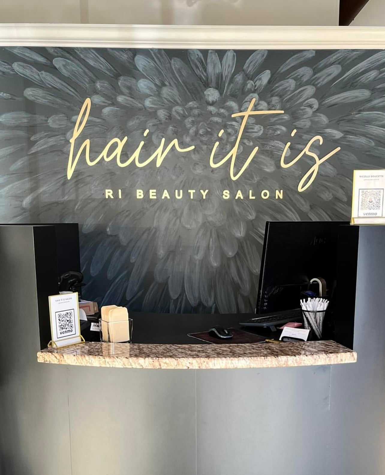 Front desk of "Hair It Is" RI Beauty Salon with check-in counter and QR code for services.