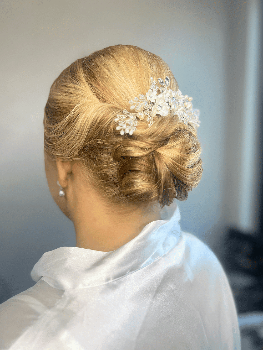 Woman with an elegant updo hairstyle adorned with a jeweled floral hair accessory, wears a white robe.