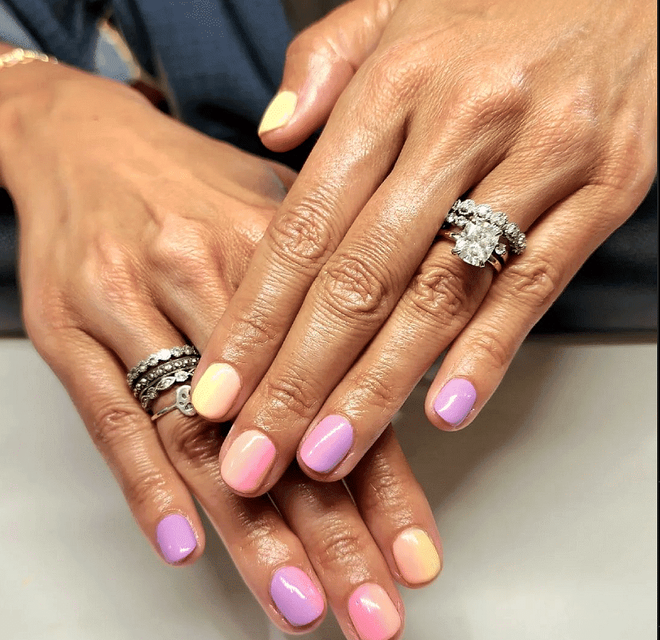 Hands with colorful, multi-shade manicured nails and several rings with gemstones.